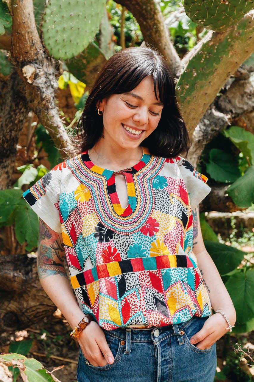 Kobieta w kolorowej haftowanej bluzce na każdą okazję przed kaktusem, uśmiechnięta, styl boho.