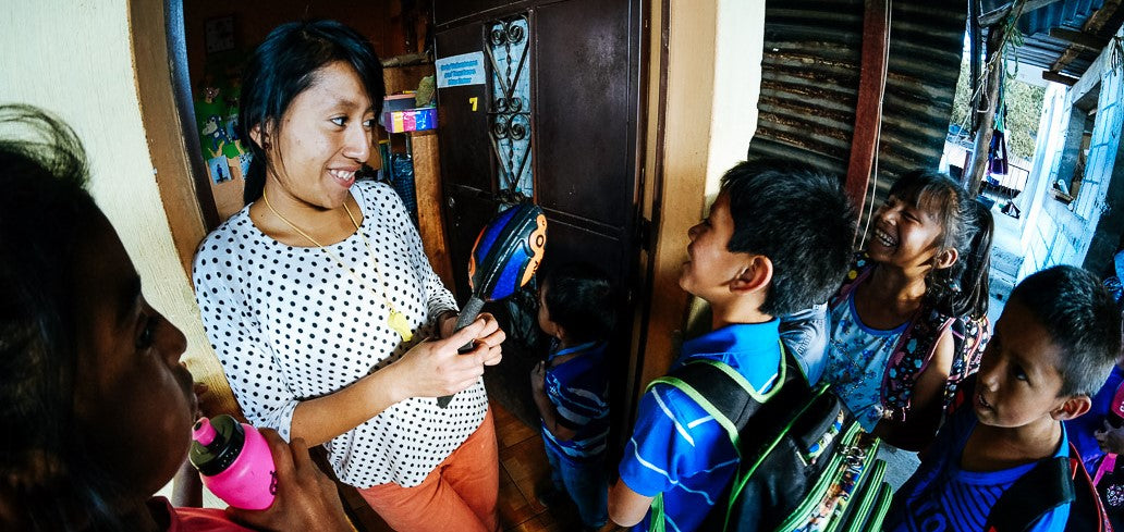 Woman distributing school supplies to children with backpacks during fundraising event for school starter kits in Guatemala